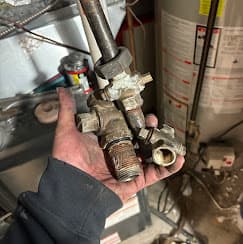 Cold Force Mechanical technician holding a brass gas valve fitting in a residential mechanical room