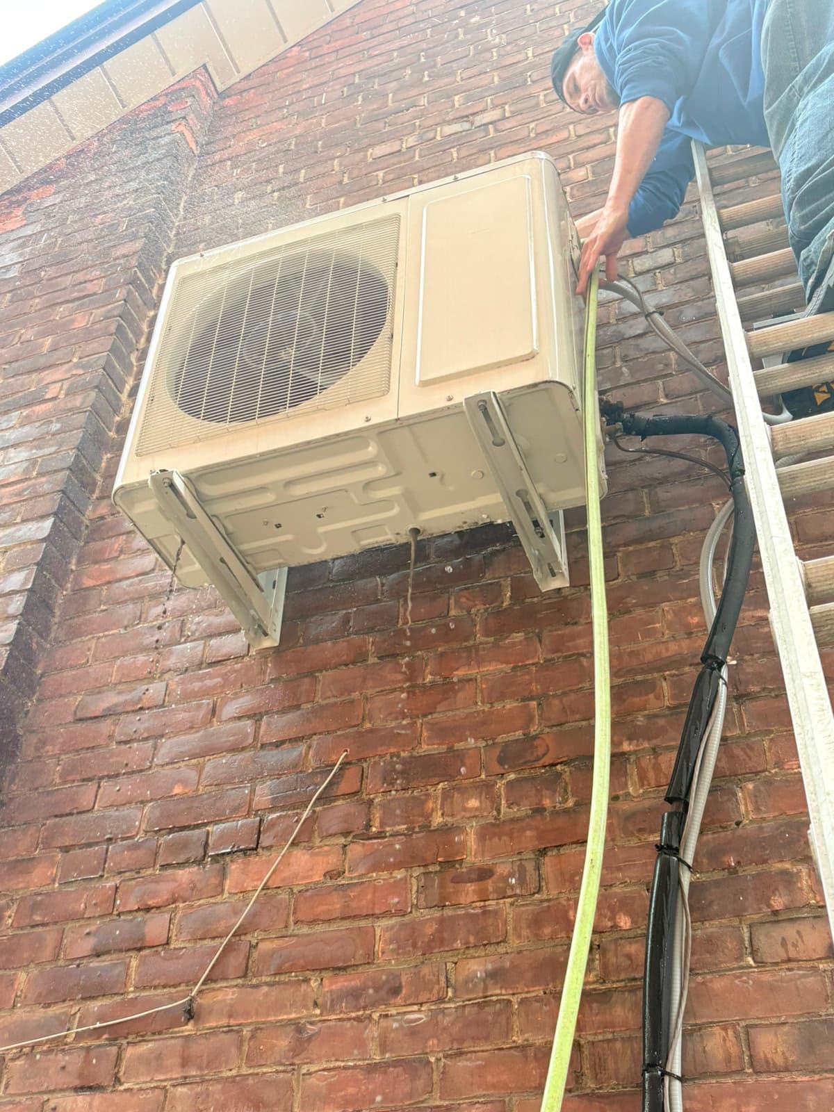 Cold Force technician on a ladder pressure-cleaning a wall-mounted mini-split outdoor unit